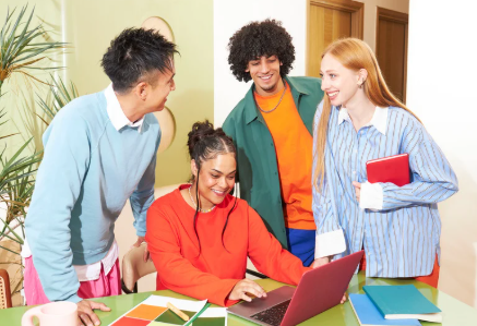 Vier Personen sind abgebildet, die miteinander lachen und sprechen. Eine Frau sitzt vor einem Laptop.
